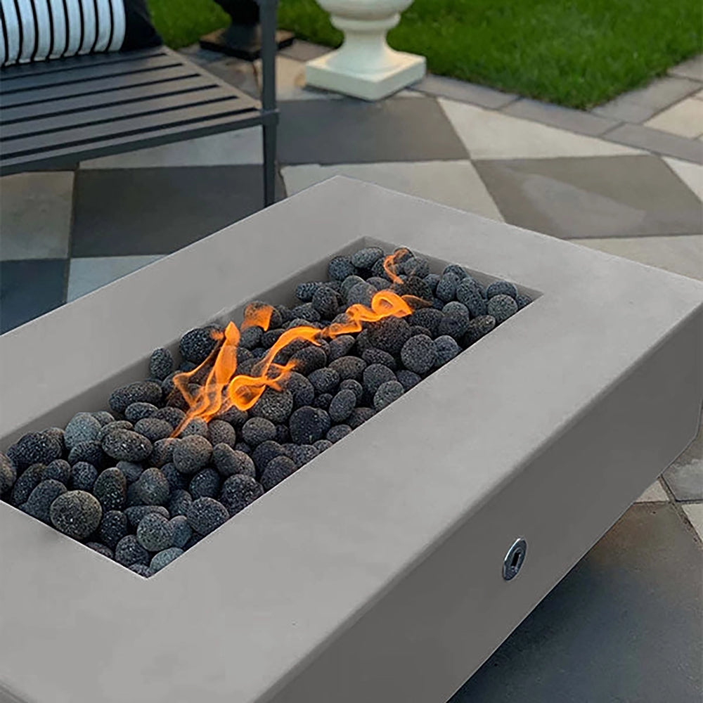 The Outdoor Plus 60-inch Del Mar Concrete Gas Fire Pit in silver, showcasing a modern and metallic-like finish that elevates any outdoor space. Equipped with a gas flame among dark stones, this fire pit is ideal for creating a contemporary ambiance in patios and backyards. A stylish gas fire pit for outdoor luxury settings