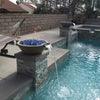 A serene outdoor pool setup featuring two Sedona Round Fire and Water Bowls by The Outdoor Plus in a smooth, earthy concrete finish. Each bowl emits a soft flame over deep blue fire glass while water gently cascades into the pool below. A nearby hammock and modern stonework create a peaceful backyard retreat perfect for relaxation and warmth.
