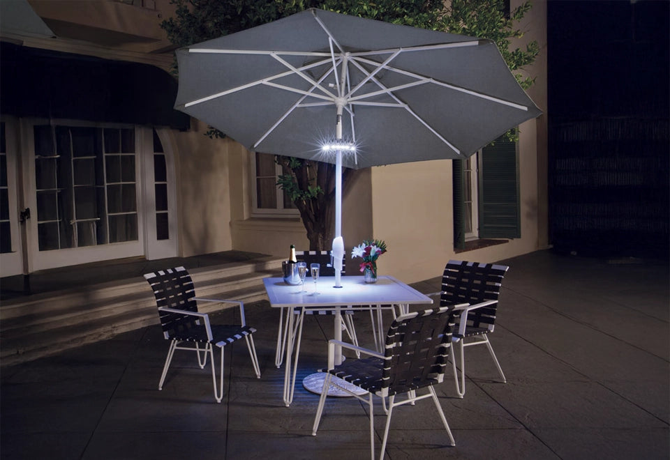 Patio dining setup with a modern gray umbrella featuring integrated LED lighting, illuminating a white dining table and contemporary black-and-white chairs for an elegant evening ambiance.