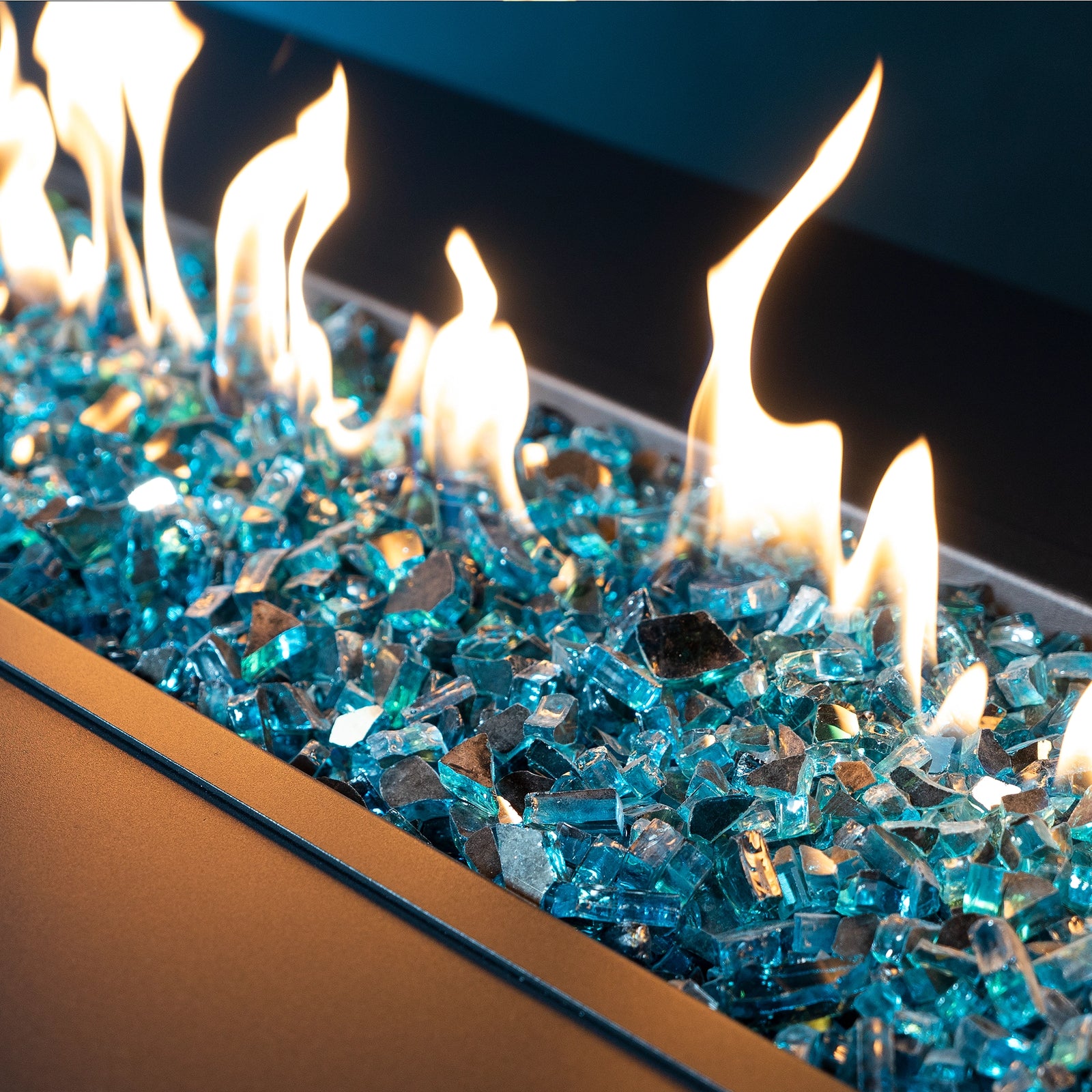 Close-up of blue fire glass with flames dancing above, set in a modern fire pit, showcasing the reflective and vibrant quality of the glass